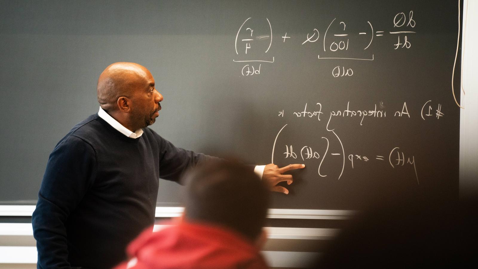 Edray Goins points to a chalkboard in a classroom.